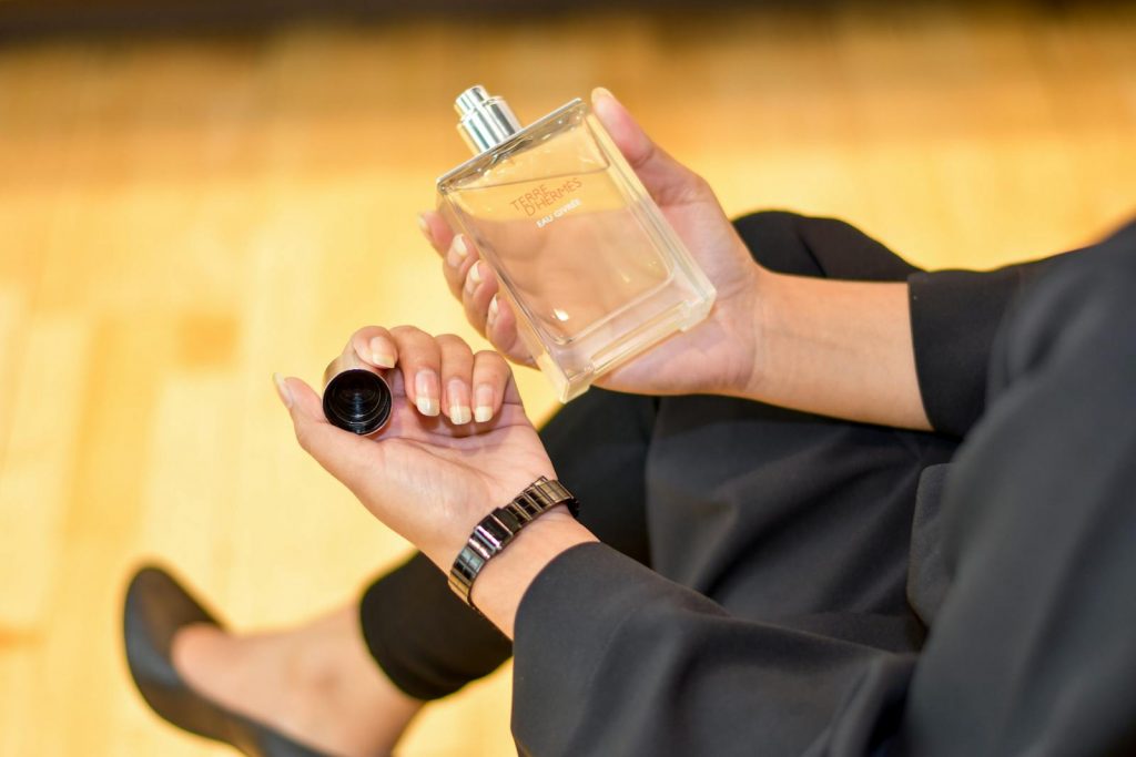 Close-up of a woman holding a Terre d'Hermes perfume bottle indoors, showcasing elegance and luxury.