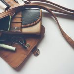 Overhead view of leather bag with eyeglasses, wallet, and smartphone laid out.